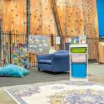 Relaxed OSHC reading nook with blue sofa, floor cushions, patterned rug, and indoor rock climbing wall backdrop.