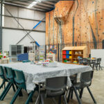 Unique OSHC space with activity tables, colourful storage, and a large indoor rock climbing wall backdrop.