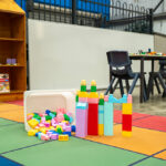Colourful building blocks on a rainbow play mat in an OSHC area, with board game shelving in the background.