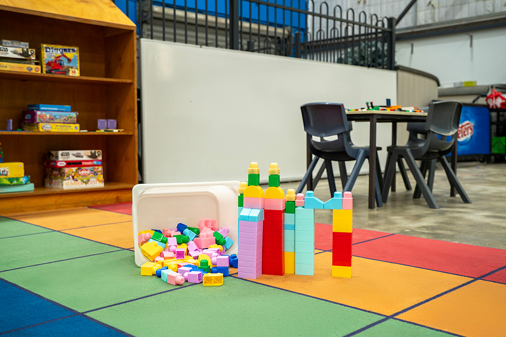 Colourful building blocks on a rainbow play mat in an OSHC area, with board game shelving in the background.