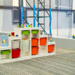 White storage shelving with colourful bins, blocks, and books in an OSHC play area, with sports balls nearby.