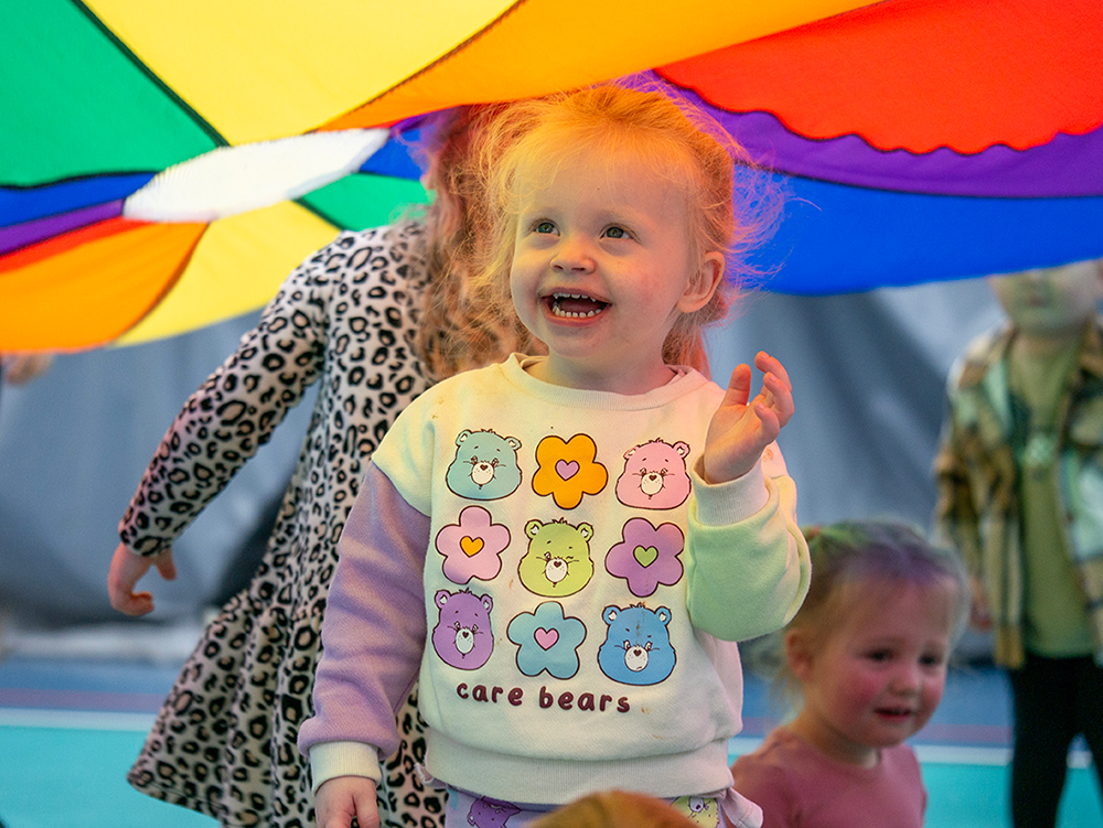 Smiling child playing underneath rainbow parachute
