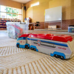 A toy truck on a rug in an OSHC play area, with storage bins and activity space in the background.