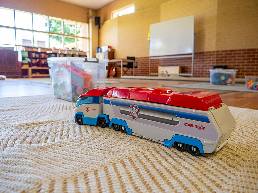 A toy truck on a rug in an OSHC play area, with storage bins and activity space in the background.
