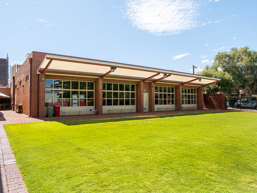 Exterior of a brick OSHC building with large windows, covered walkway, and manicured green lawn.