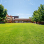 Spacious green oval with mature trees, OSHC building, and covered outdoor area in the background.