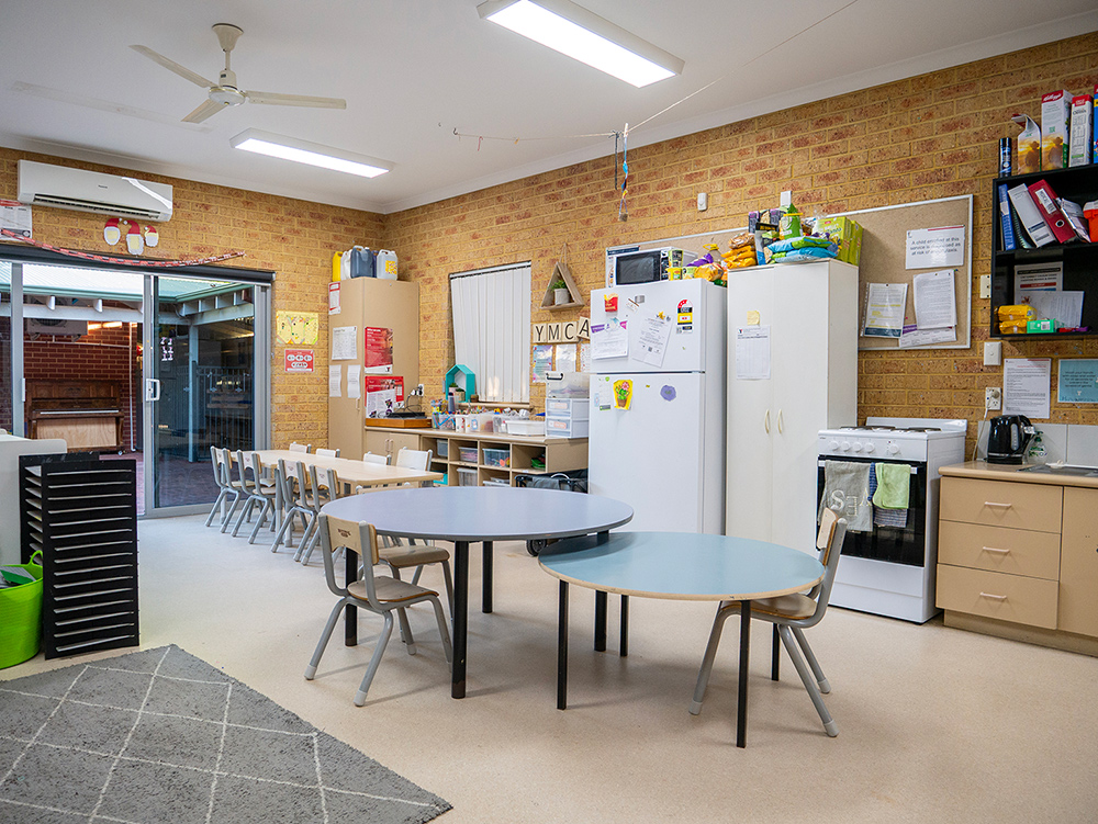 Spacious Y WA OSHC room with round tables, chairs, kitchen area, and open door to outdoor space.