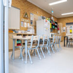 Y WA OSHC activity room with long tables, chairs, storage shelving, fridge, and brick feature wall.