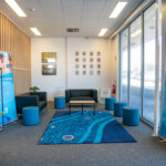 A welcoming Y School reception area featuring a seating area with an Aboriginal-designed rug, framed photos on the wall, indoor plants, and Y School informational banners