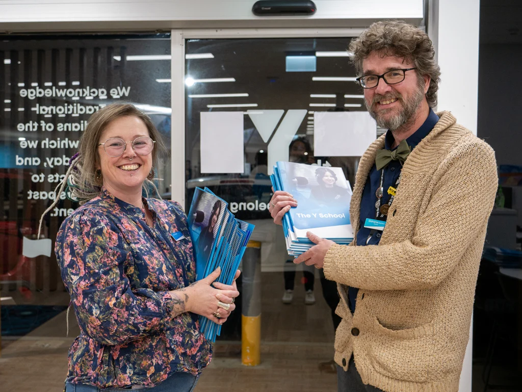 Two Y School staff members standing at the front of the Junior Y School Mirrabooka Campus with booklets to welcome new parents