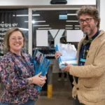 Two Y School staff members standing at the front of the Junior Y School Mirrabooka Campus with booklets to welcome new parents