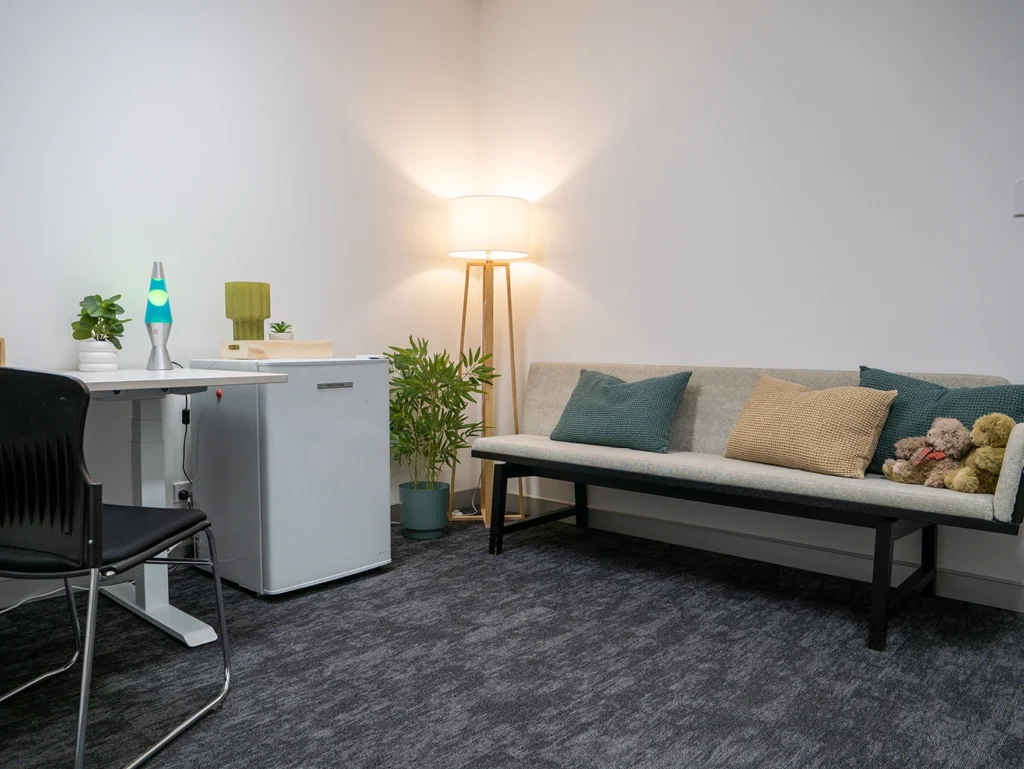 A cosy corner at the Y School with a couch, table, warm lighting and plants. There is also a lava lamp on the desk