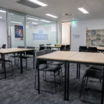 Large classroom at Y School Mirrabooka Junior Campus, featuring four tables and chares with a bookshelf in the back and artwork on the walls
