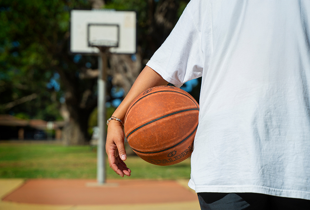 Close up of young person holding a basketball on an outside basketball court