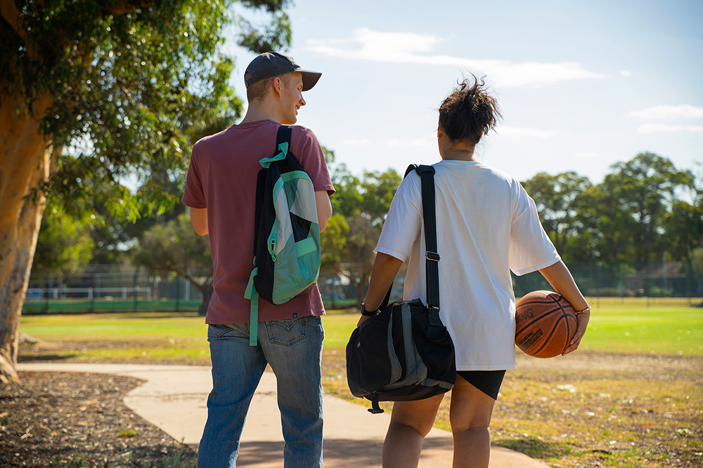 Two young people walking away from basketball court after playing together