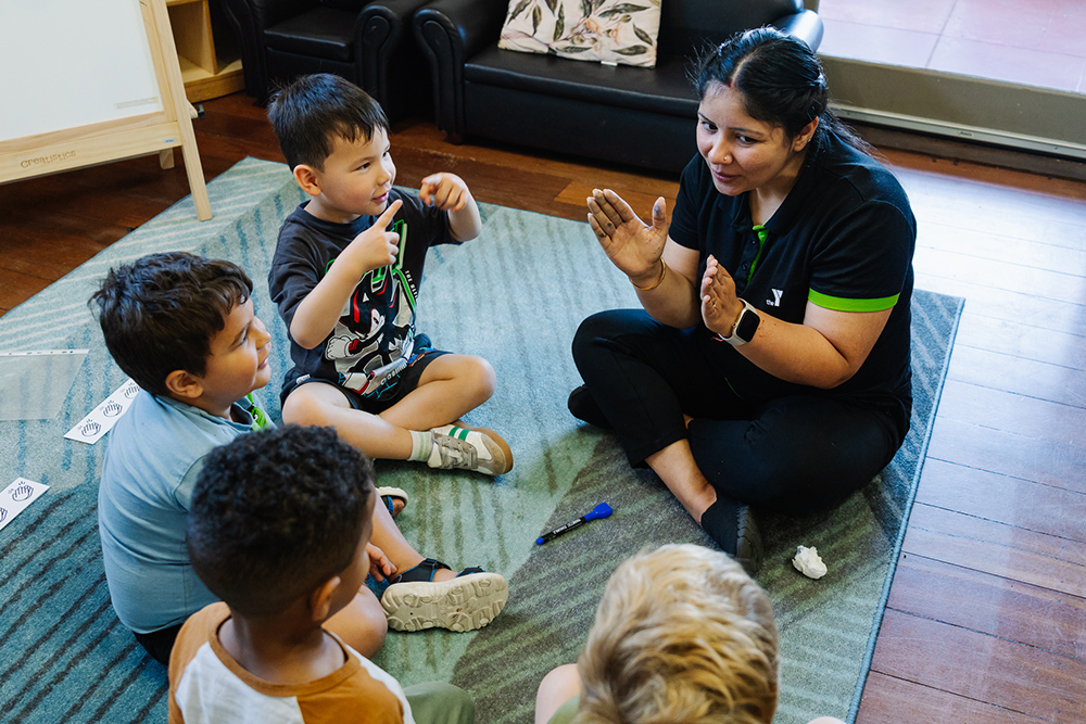 Educator and group of children engaging together on carpet at childcare centre.