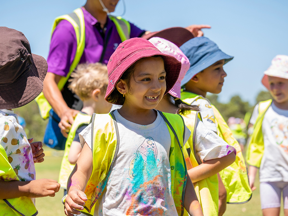 Smiling child in pink sun hat and safety vest on supervised outdoor excursion with group