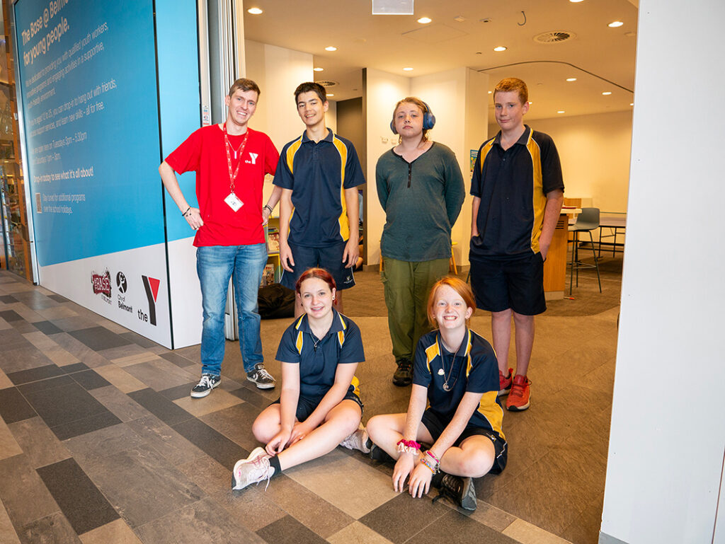 A Y WA youth worker in a red shirt poses with a group of five teenagers at a youth drop-in centre