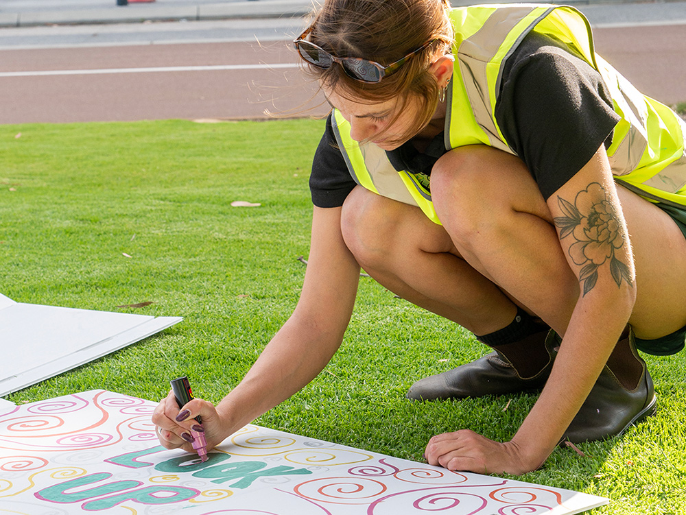 A Y WA youth worker colouring in a cardboard sign outside using POSCA paint pens