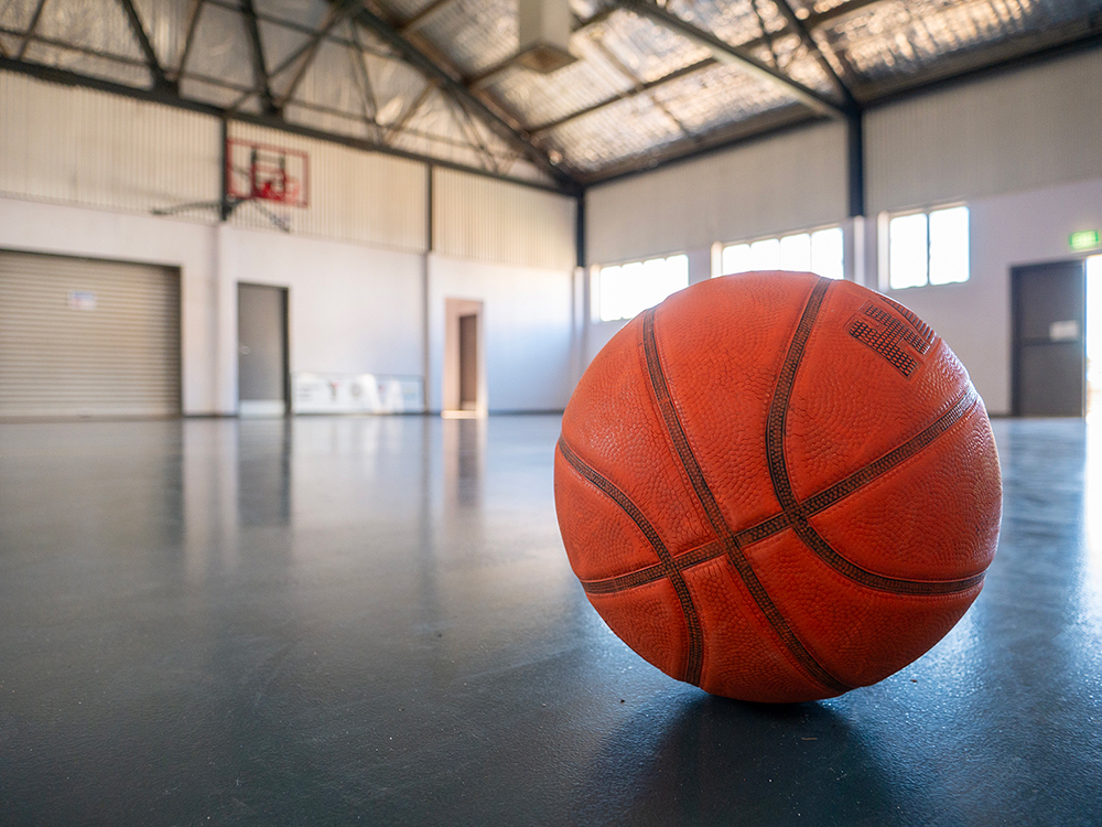 A close up image of a basketball won the floor of a large indoor basketball court