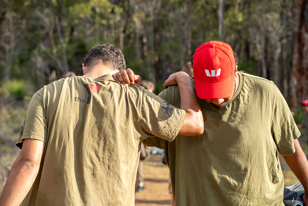 Two young people stretching together outside while wearing a Y WA tshirt and Westpac hat
