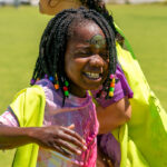 A young girl laughs with joy, face wet and decorated with a sticker, during an outdoor water play activity