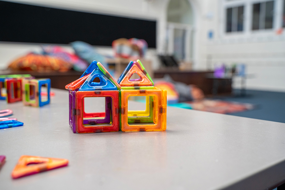 Colourful magnetic tiles assembled into two small house shapes on a table in a children's play space