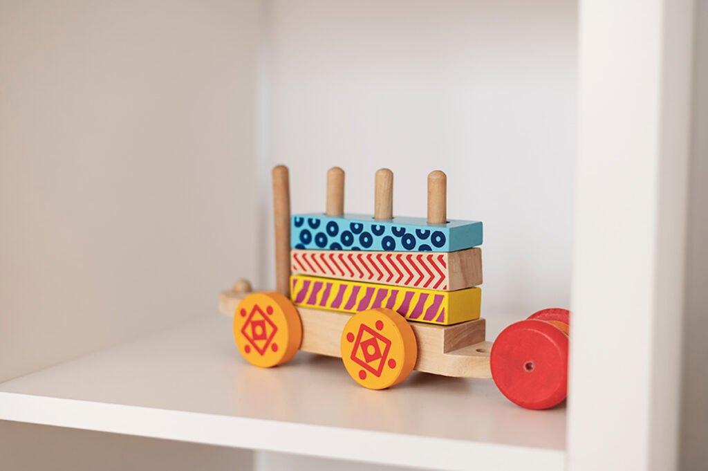 A colourful wooden stacking toy train with patterned blocks sits on a white shelf
