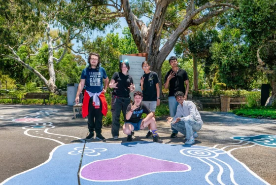 Group of young people standing on top of street art painted on the footpath in a park.