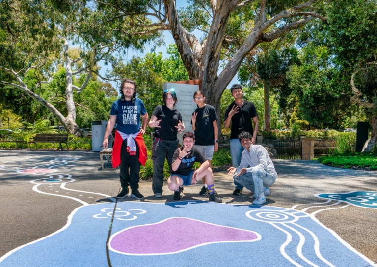 Group of young people standing on top of street art painted on the footpath in a park.