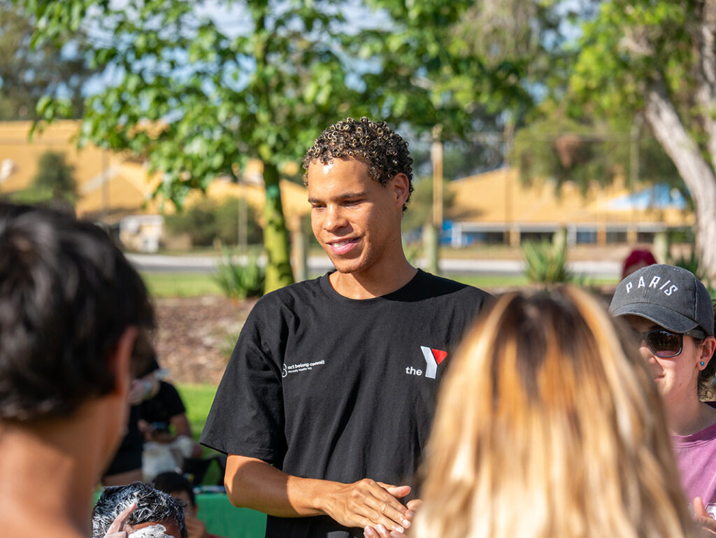 A smiling Y WA staff member in a black t-shirt talks with community members at an outdoor event