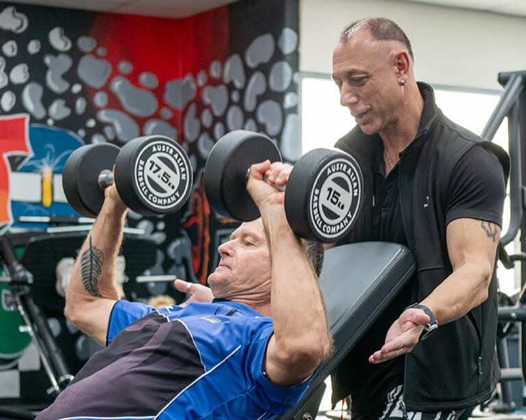 A personal trainer spots an older man performing a barbell squat in a gym weight room
