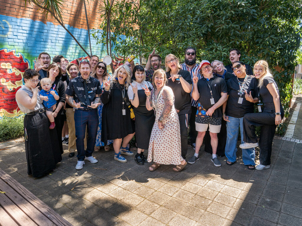 Group image of Y School staff including teachers, youth workers, and leadership standing outside in front of a graffiti wall