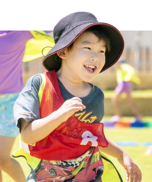 Happy child in sun hat with a red mesh vest on during outdoor play activity