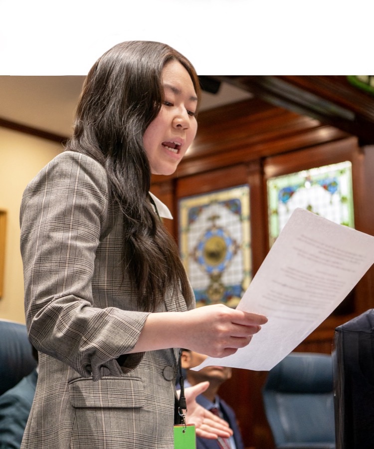 Young woman delivering speech with document at youth parliamentary event