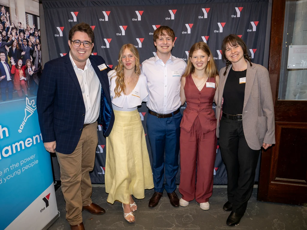 Group of young people who make up part of the youth parliament alumni, standing in front of Y branded signage