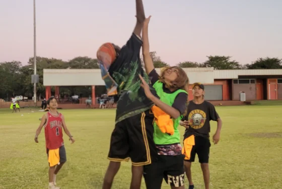 two young people jumping up for a football on a green oval outside