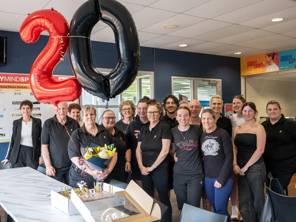 Staff from serpentine jarrahdale rec centre standing together behind a '20' balloon and cake to celebrate Kate Kings 20 years with the Y WA